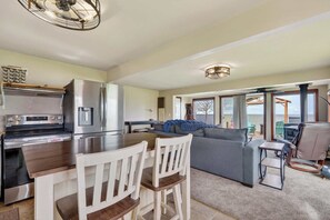 A modern kitchen with a central island, a dining area with chairs, a sofa, and a view of the sea.
