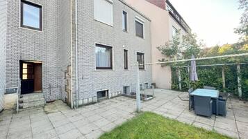 Um edifício residencial com fachada de tijolos, porta visível e área de pátio com mesa e cadeiras.