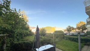 Een terras buiten met een tafel en stoelen, omgeven door groen en een uitzicht op gebouwen in de verte.