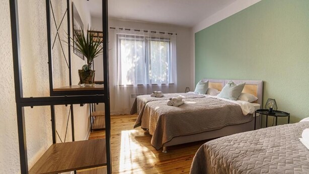 Een slaapkamer met twee bedden, een houten vloer, een groene wand en een raam met gordijnen.