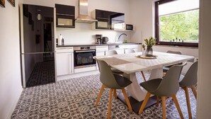 Een moderne keuken met witte kasten, een eettafel met stoelen en een raam met uitzicht op groen.