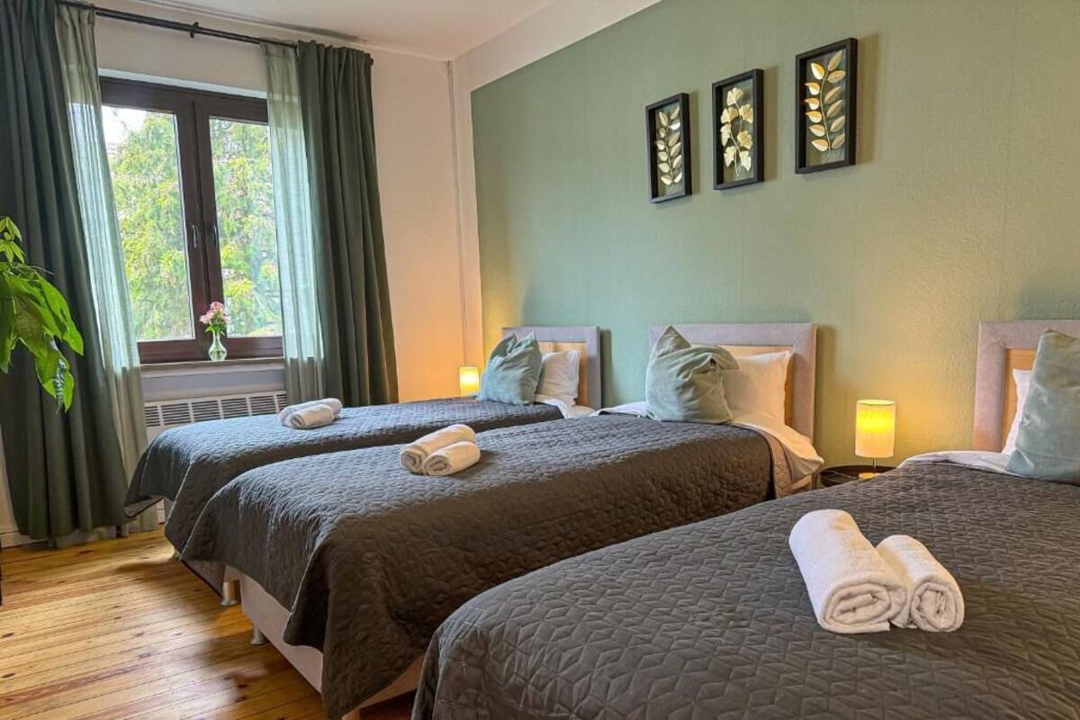 Ein Hotelzimmer mit zwei Betten, einem Fenster mit Vorhängen, einer Pflanze und Wandbildern.