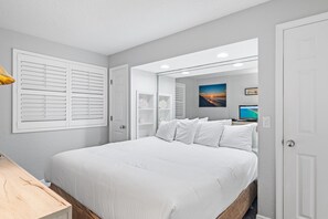 Ein Schlafzimmer mit einem großen Bett, einem Nachttisch, einem Spiegel und einem an der Wand befestigten Fernseher.