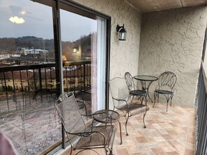 Ein Balkon mit Metallstühlen und einem Tisch, Blick auf Gebäude und eine Straße, sowie eine strukturierte Wand.