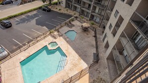 Una piscina en la azotea con un pequeño jacuzzi, rodeada por una terraza de piedra y una valla metálica.
