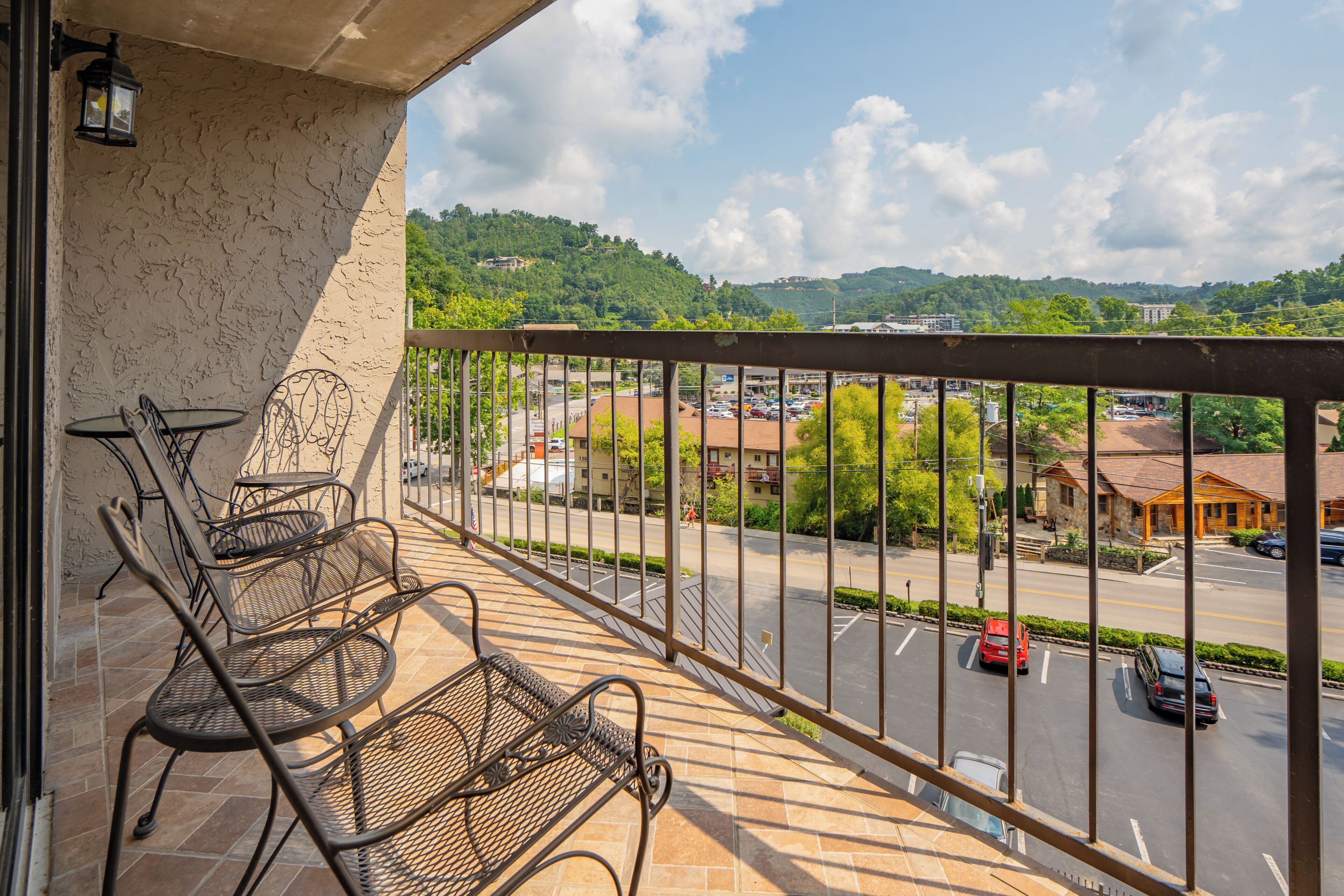 Ein Balkon mit Metallstühlen und einem Tisch, mit Blick auf eine Straße mit Autos und Gebäuden.