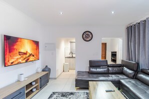 Ein modernes Wohnzimmer mit einer Ledersofa, einem Flachbildfernseher, einem Couchtisch aus Holz und einer Küche im Hintergrund.