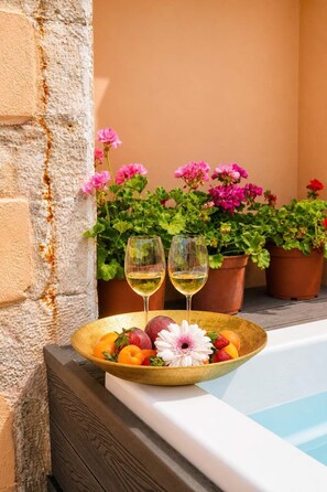 Ein Poolbereich mit Obstschale, zwei Gläsern Weißwein und Topfpflanzen mit rosa Blüten.