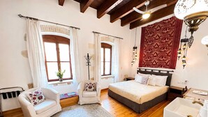 Une chambre à coucher comprenant un lit, une chaise, une table de chevet, une commode, une fenêtre et une lampe fixée au mur.