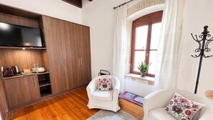 Un salon comprenant un canapé, un fauteuil, un téléviseur, un plancher en bois, une fenêtre avec des rideaux et une plante.