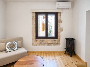 Ein Zimmer mit Steinwand, Fensterläden, einem Sofa mit Zierkissen, einem runden Holztisch und einem dunklen Holzschrank.