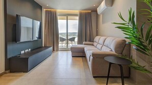 Ein modernes Wohnzimmer mit Flachbildfernseher, einer Couch, einem kleinen Tisch und einem großen Fenster mit Vorhängen.