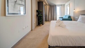 Ein Hotelzimmer mit einem großen Bett, einem Blumentopf, einem Sessel und Blick ins Freie.