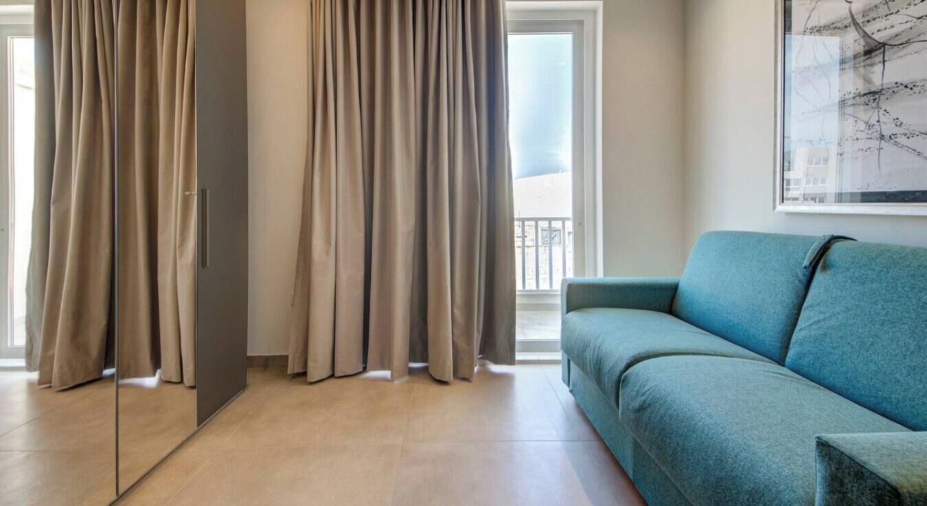 A living room with a sofa, curtains, and a window.