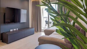 Ein modernes Wohnzimmer mit einem an der Wand befestigten Flachbildfernseher, einem dunklen Konsolentisch, einem beige farbenen Sofa und einer großen Zimmerpflanze.