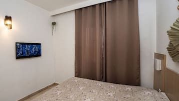 Una habitación de hotel con cama, televisor de pantalla plana, lámpara de pared y cortina.