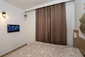A hotel room with a bed, a flat-screen TV, a wall-mounted light, and a curtain. - SHB - Family 2 Suítes Piscina e Academia (Santos)