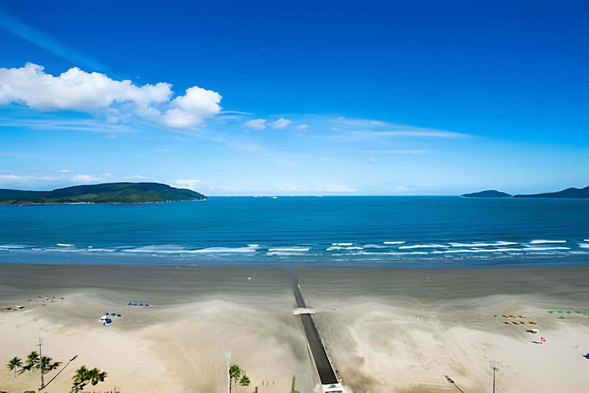 A beach with a long pier extending into the ocean, surrounded by clear skies and distant islands.