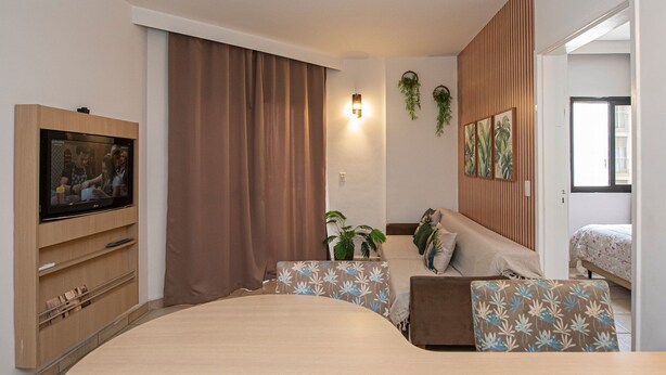 Un dormitorio moderno con una cama grande, un televisor sobre un mueble de madera y una pequeña zona de escritorio.