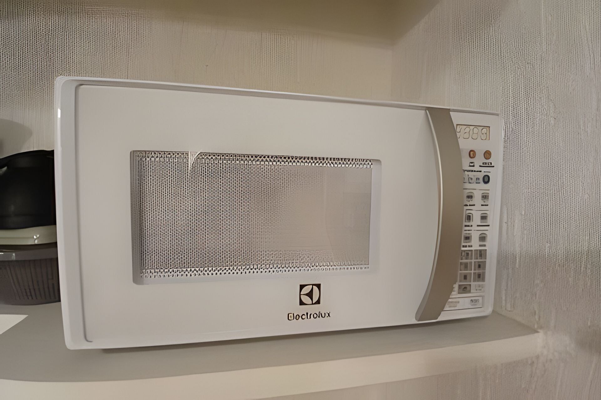Un four à micro-ondes blanc, doté d’un écran numérique et d’un panneau de commande, est posé sur une étagère blanche.