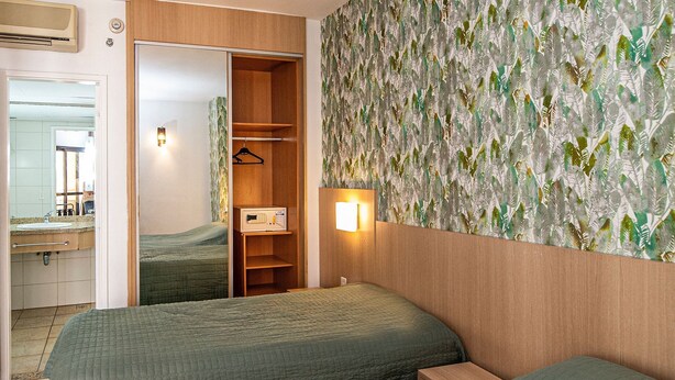 Quarto com duas camas, um guarda-roupa, um espelho e uma luminária na parede.