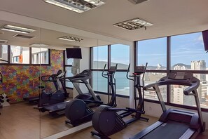Un gimnasio con cintas de correr, elípticas y un mural colorido en la pared.