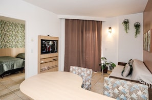 A living room with a TV, a sofa, a dining table, and a bed. - SHB - Family 2 Suítes Piscina e Academia (Santos)
