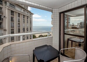 A balcony with a view of the ocean, a tiled wall, and a small table and chair. - SHB - Family 2 Suítes Piscina e Academia (Santos)