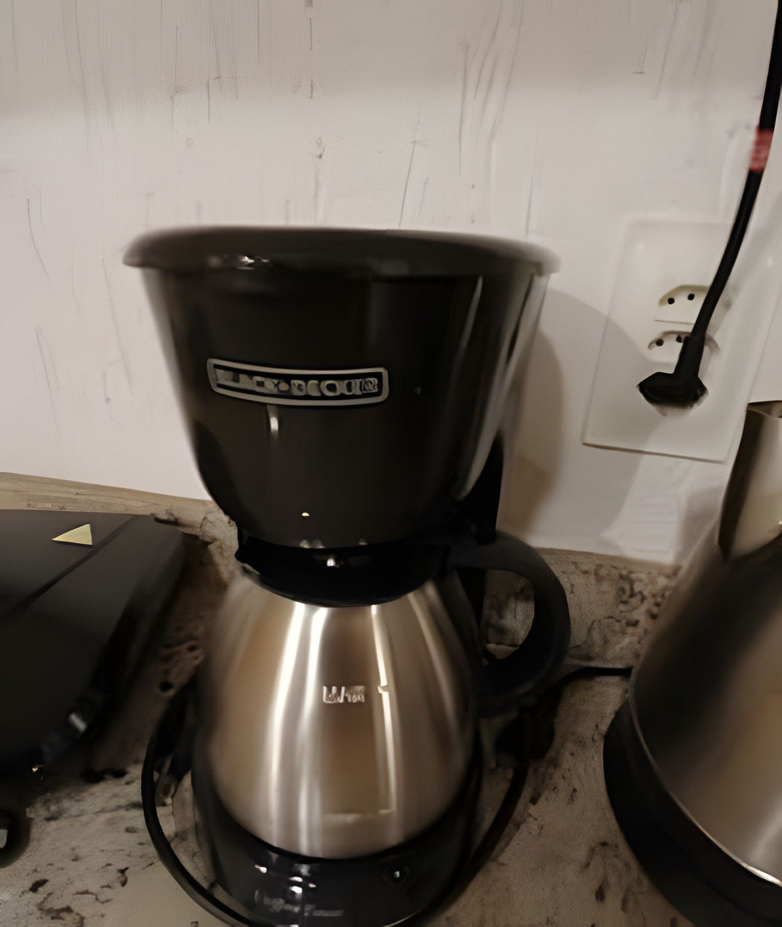 Een koffiezetapparaat met een zwart en zilveren ontwerp, geplaatst op een aanrecht naast een witte stopcontact.