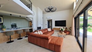 Een moderne woonkamer met een modulaire bank, een eethoek met barkrukken, een open haard en een grote televisie.
