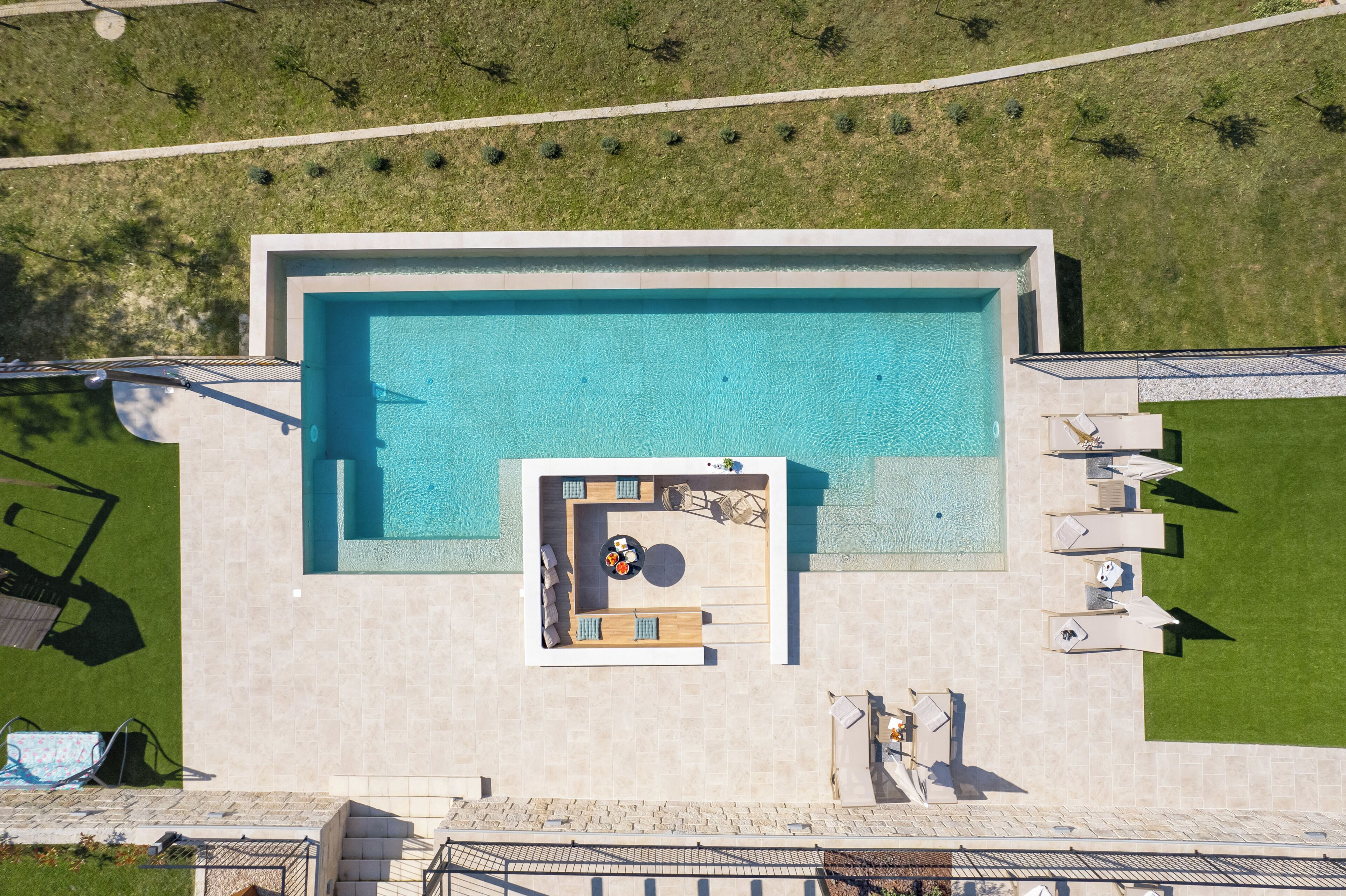 Vista aérea de una piscina rectangular con solárium y sillones de descanso.