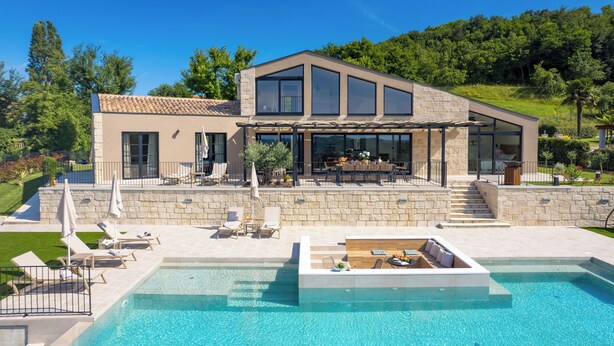 Een modern huis met zwembad, buitenmeubilair en een stenen gevel.