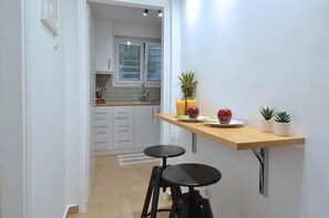 Une cuisine avec un plan de travail en bois, deux tabourets et une petite table sur laquelle on trouve des fruits et un ananas.