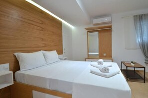 Une chambre d’hôtel avec une tête de lit en bois, un lit avec du linge de maison blanc, une table de chevet avec une lampe et une petite table avec des serviettes.