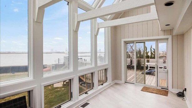 Una habitación amplia con ventanas grandes, un ventanal corredero que da a una terraza exterior y un techo alto con vigas a la vista.