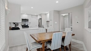 Una cocina moderna con muebles blancos, una isla central y una zona de comedor con sillas a rayas.