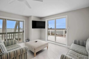 A spacious room with a large sliding glass door leading to an outdoor balcony, a flat-screen TV mounted on the wall, and two striped sofas. - Bay front Sunsets in Brigantine - Boat Dock & Deck (Brigantine)