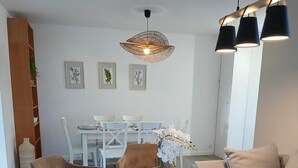 Een moderne woonkamer met een bank, twee fauteuils, een salontafel, een eettafel met stoelen en een hanglamp.