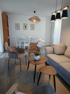 A modern living room with a sofa, two armchairs, a coffee table, a dining table with chairs, and a hanging light fixture. - Ti ar Mor Bihan (Riantec)