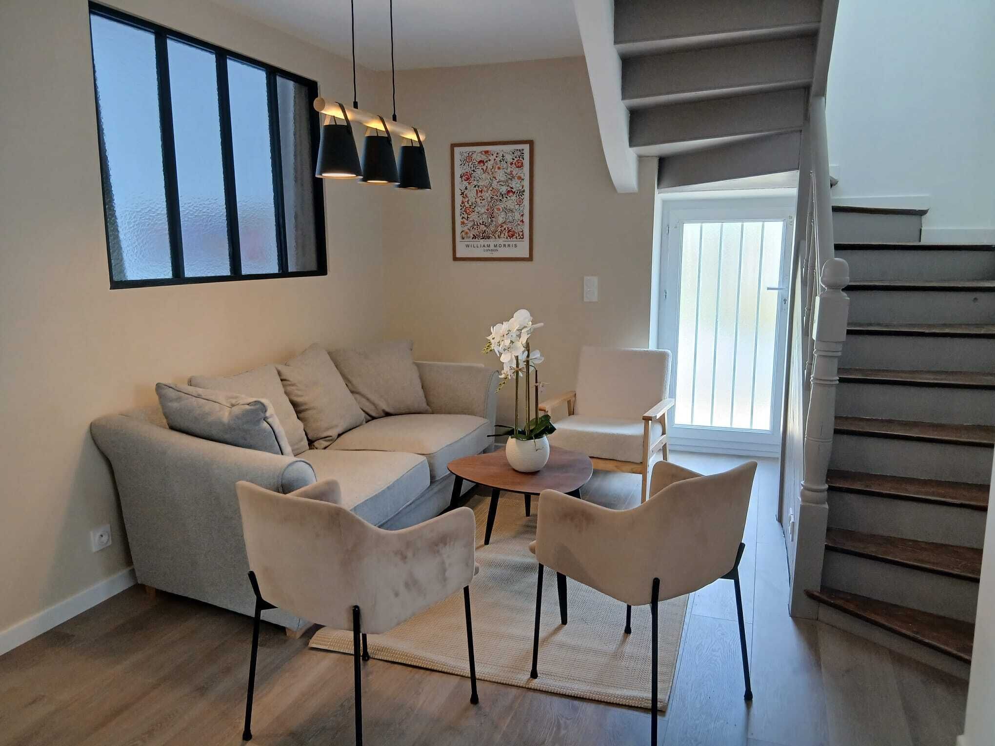 A living room with a sofa, two chairs, a coffee table, a vase with flowers, a painting, and a staircase.