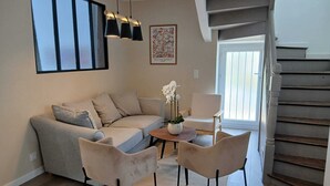 Een woonkamer met een bank, twee stoelen, een salontafel, een vaas met bloemen, een schilderij en een trap.