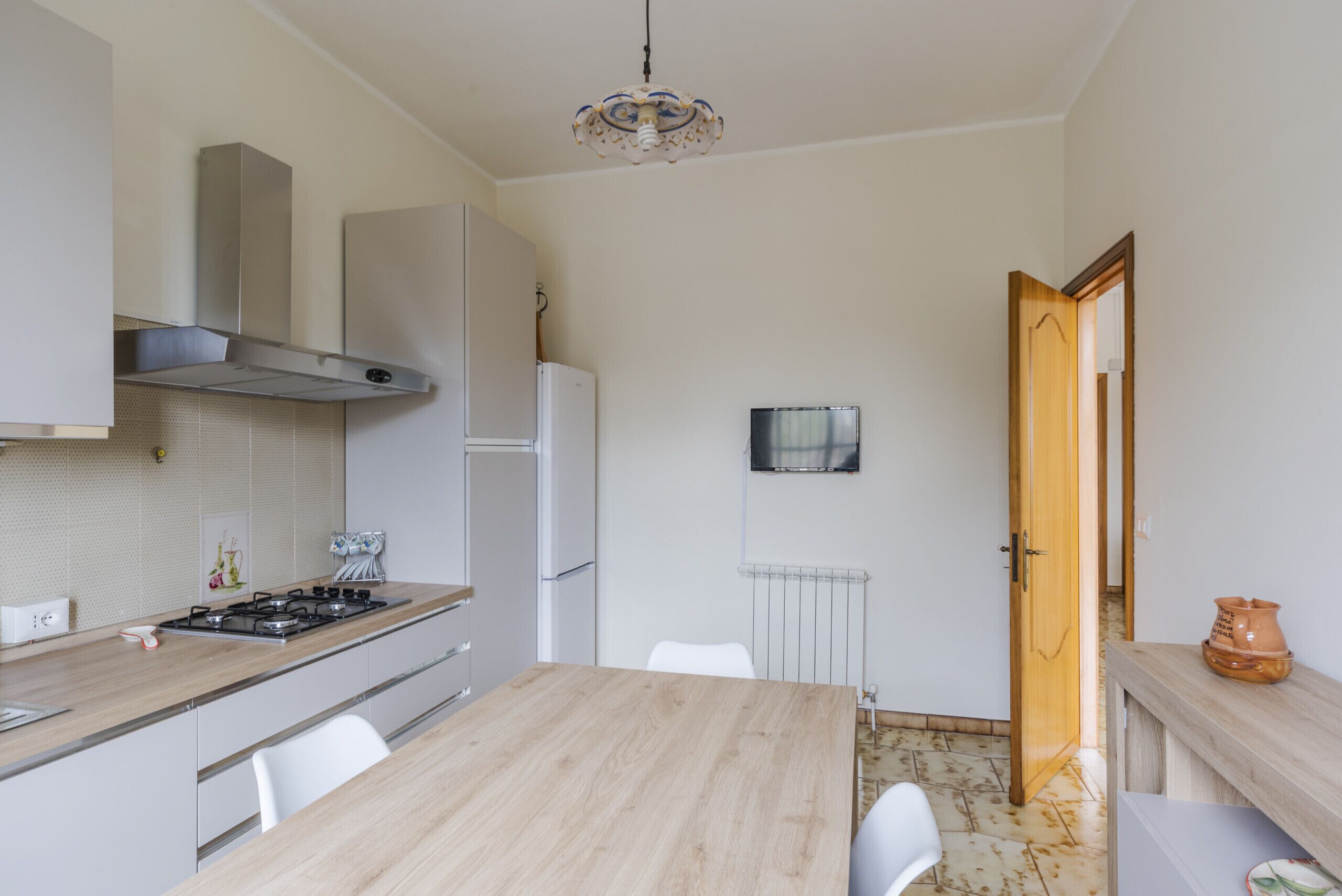 Une cuisine moderne dotée d’un plan de travail en bois, de meubles blancs, d’une hotte en acier inoxydable, d’un réfrigérateur blanc et d’un coin repas avec une table et des chaises en bois.