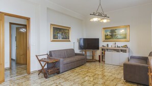 En stue med sofa, fjernsyn, skab i træ og to billeder på væggen.