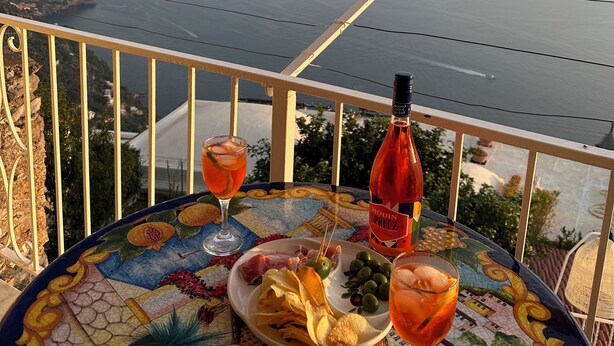 A table with a bottle of Modin Spritz, a plate of chips, olives, and a glass of drink, overlooking a coastal view. - Casa degli Dei, Nocelle-Positano (Nocelle)