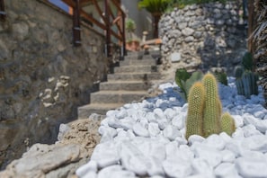 Eine Steintreppe führt zu einer Holztür, umgeben von weißen Kieselsteinen und Kakteen.