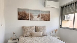 Een slaapkamer met een bed, twee nachtkastjes, een lamp, een wandairconditioner en een raam met jaloezieën.