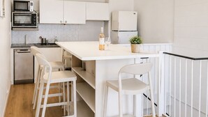 Een moderne keuken met witte kastjes, een centraal eiland, barstoelen, een magnetron, een koelkast en een plafondlamp.