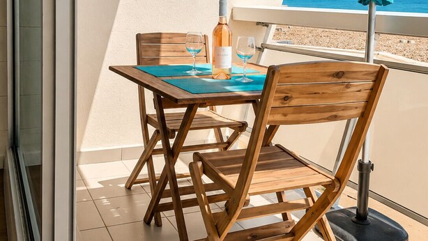 Een houten tafel en stoelen op een balkon, met uitzicht op zee.