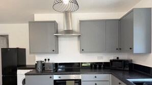 Een moderne keuken met grijze kastjes, een roestvrijstalen afzuigkap, een inbouwoven, een magnetron en een wasmachine.