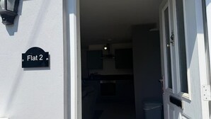 Een hal die leidt naar een keuken, met een zichtbare deur, een lamp en een bordje met daarop 'Flat 2'.
